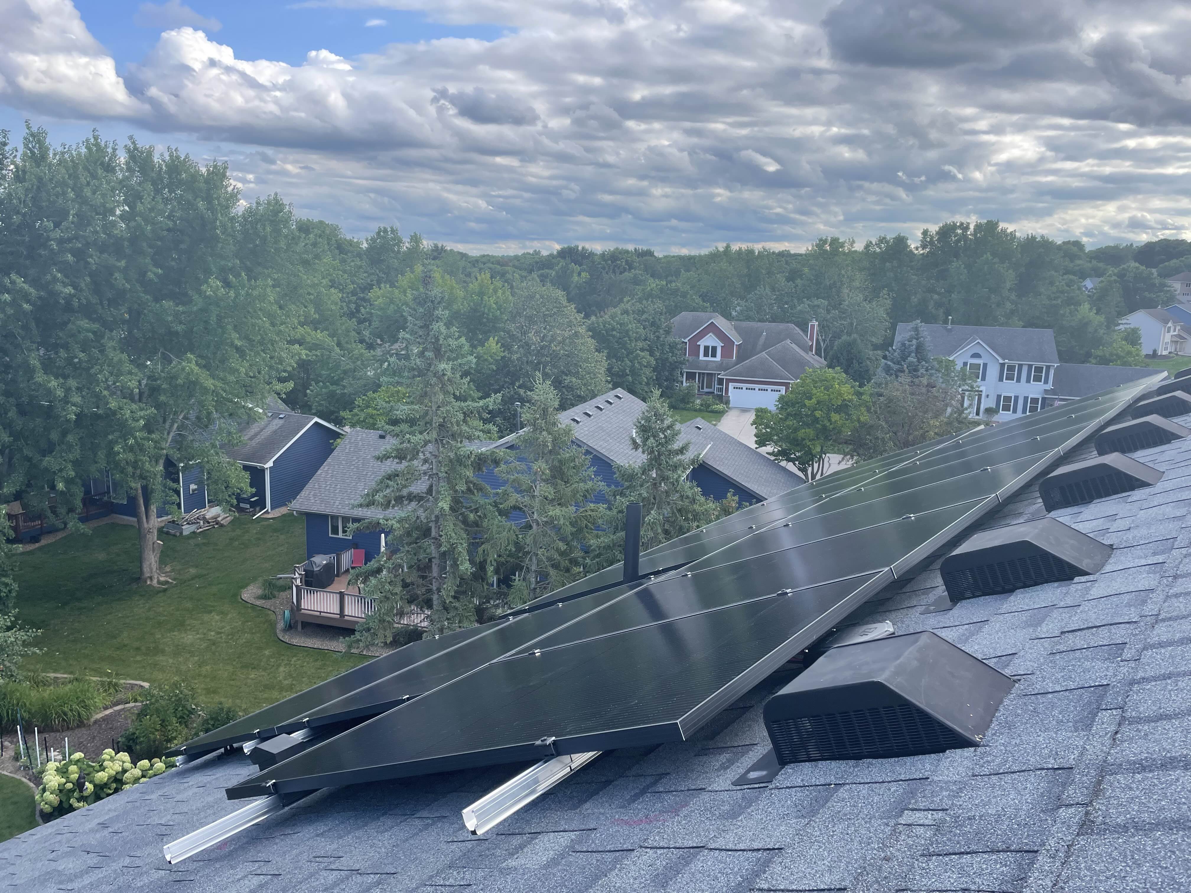 Solar panels installed on a roof with green trees viewed at an angle